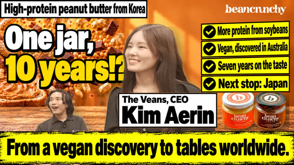 The Veans CEO Kim Aerin smiling at a sunny café table with peanut butter toast and peanuts, interviewer Kaito Ogasawara laughing beside her. Text: High-protein peanut butter from Korea. One jar, 10 years!? From a vegan discovery to tables worldwide. Four checklist tags, two BeanCrunchy jars and the logo